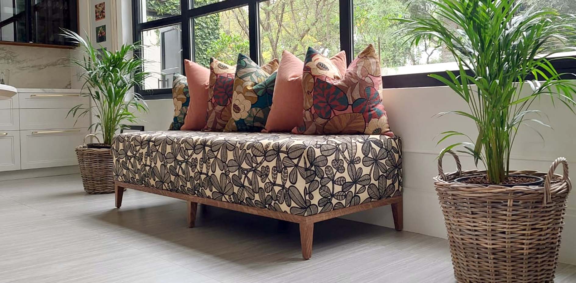 Handcrafted bench featuring patterned **bespoke upholstery** and a collection of floral and solid peach **custom cushions** in a light filled Johannesburg home.