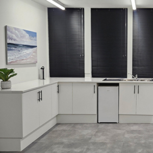 A professional medical consultation room featuring custom white cabinetry, integrated clinical storage, and architectural blinds designed by edge.ids.
