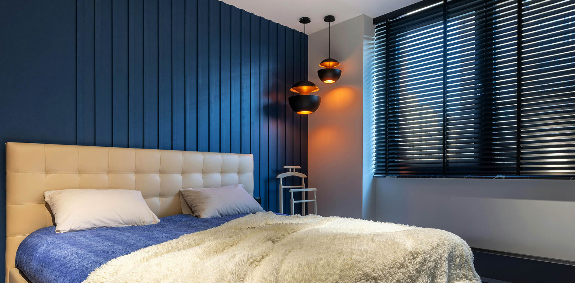 Modern bedroom featuring a blue slatted feature wall, black Venetian blinds, and warm spherical pendant lighting.