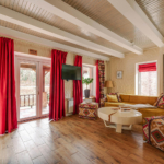 Warm residential lounge with exposed ceiling beams, red drapery, and patterned textiles showcasing intentional spatial layering.