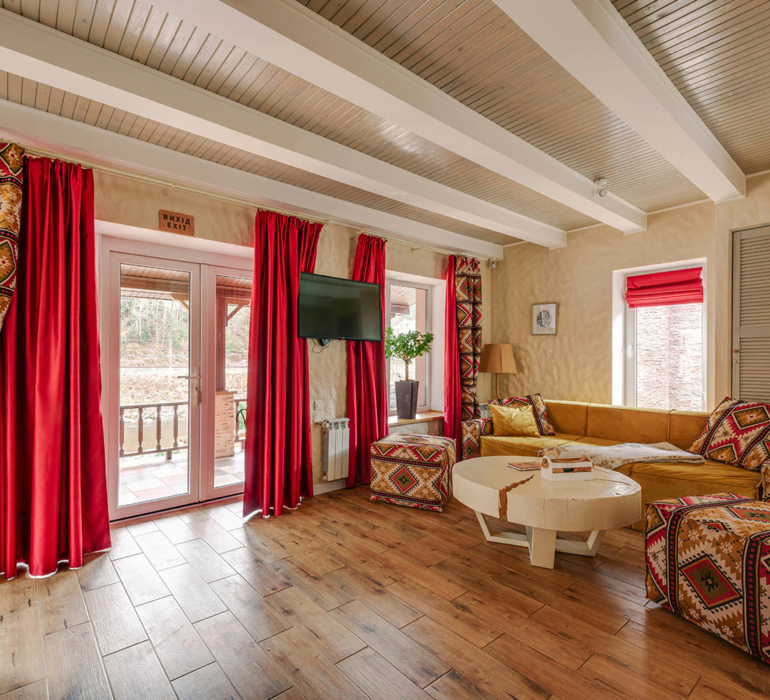 Warm residential lounge with exposed ceiling beams, red drapery, and patterned textiles showcasing intentional spatial layering.