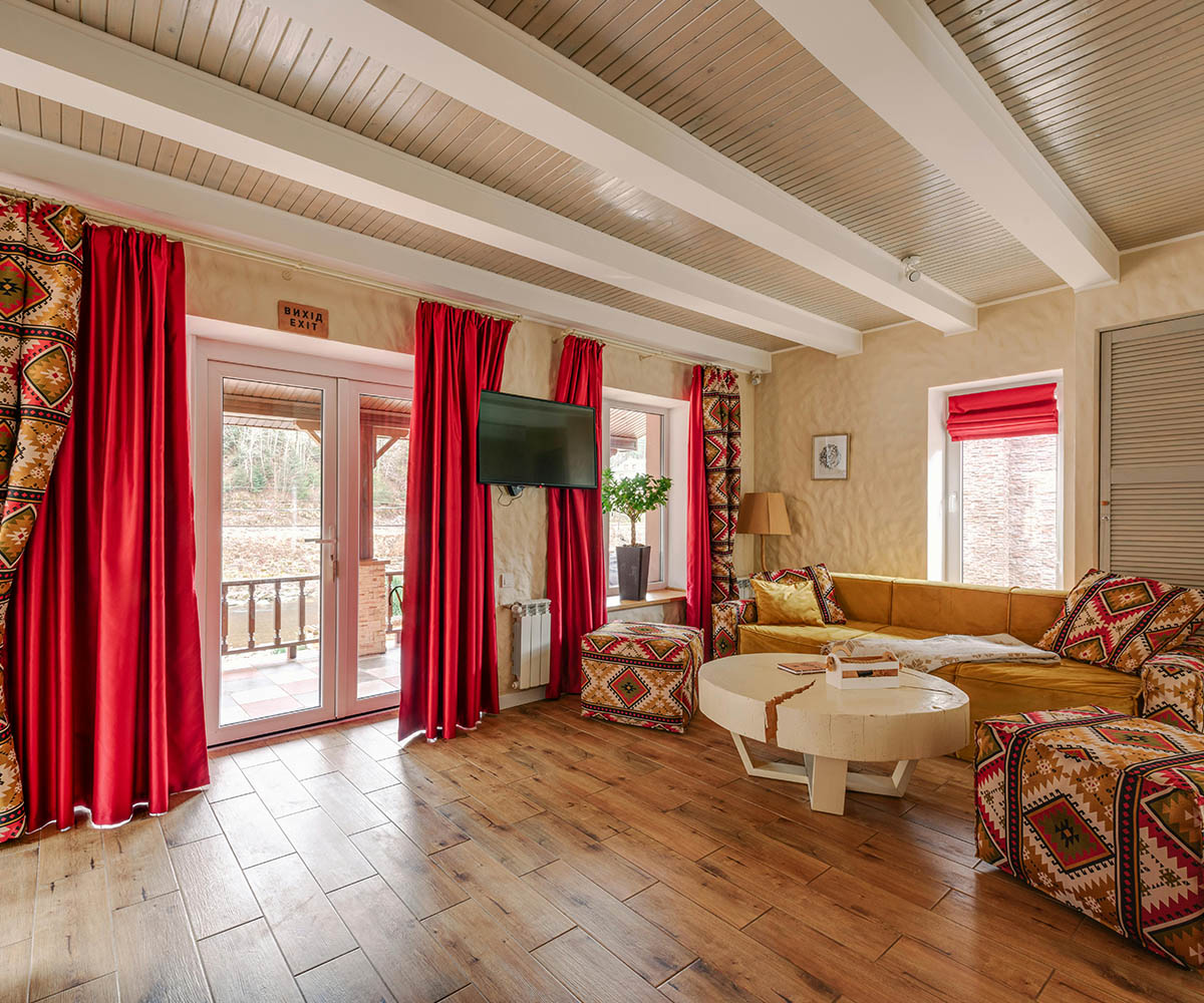Warm residential lounge with exposed ceiling beams, red drapery, and patterned textiles showcasing intentional spatial layering.
