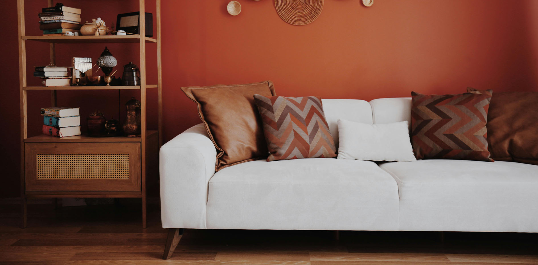 Contemporary white sofa with patterned cushions against a terracotta feature wall and custom timber shelving.