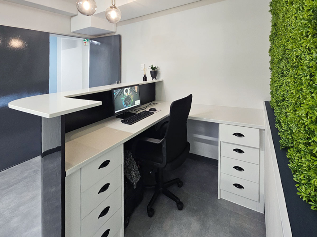 Back view of a modern medical reception desk featuring custom white cabinetry with black handles, a stone worktop, integrated green wall, and a curved privacy screen.