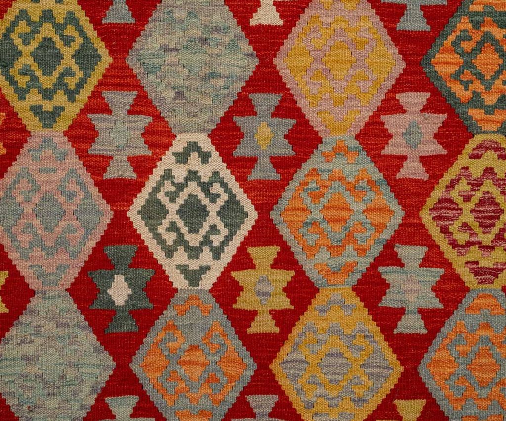 Close up of a woven kilim textile with geometric diamond patterns in red, gold, and blue.