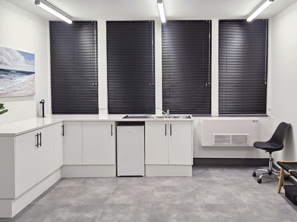 Medical suite preparation area with custom white cabinetry, black hardware, an integrated clinical sink, and black venetian blinds.