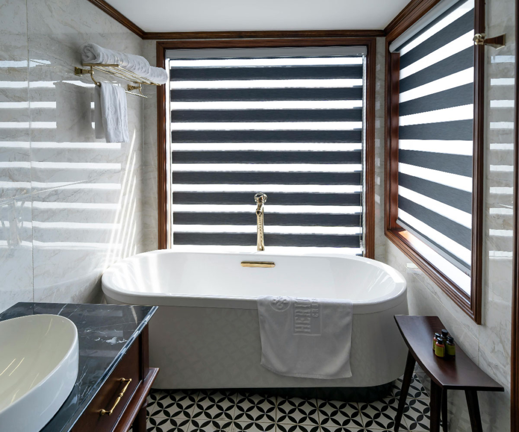 Luxury bathroom with a freestanding tub, gold fixtures, and black-and-white zebra blinds for adjustable light and privacy.