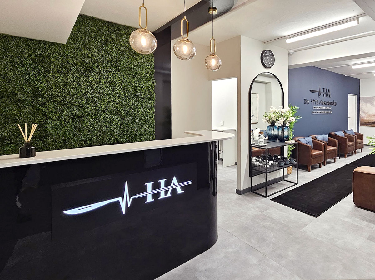Modern medical reception with a black gloss desk featuring a backlit LED logo, a large green living wall, and warm globe pendant lighting.