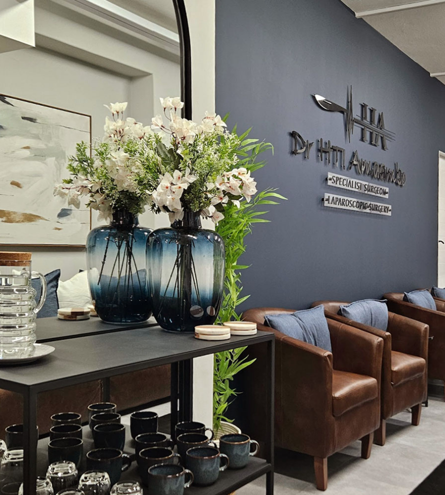 Reception waiting area of a private medical suite featuring brown leather armchairs, a navy blue feature wall with 3D signage, and a coffee station.