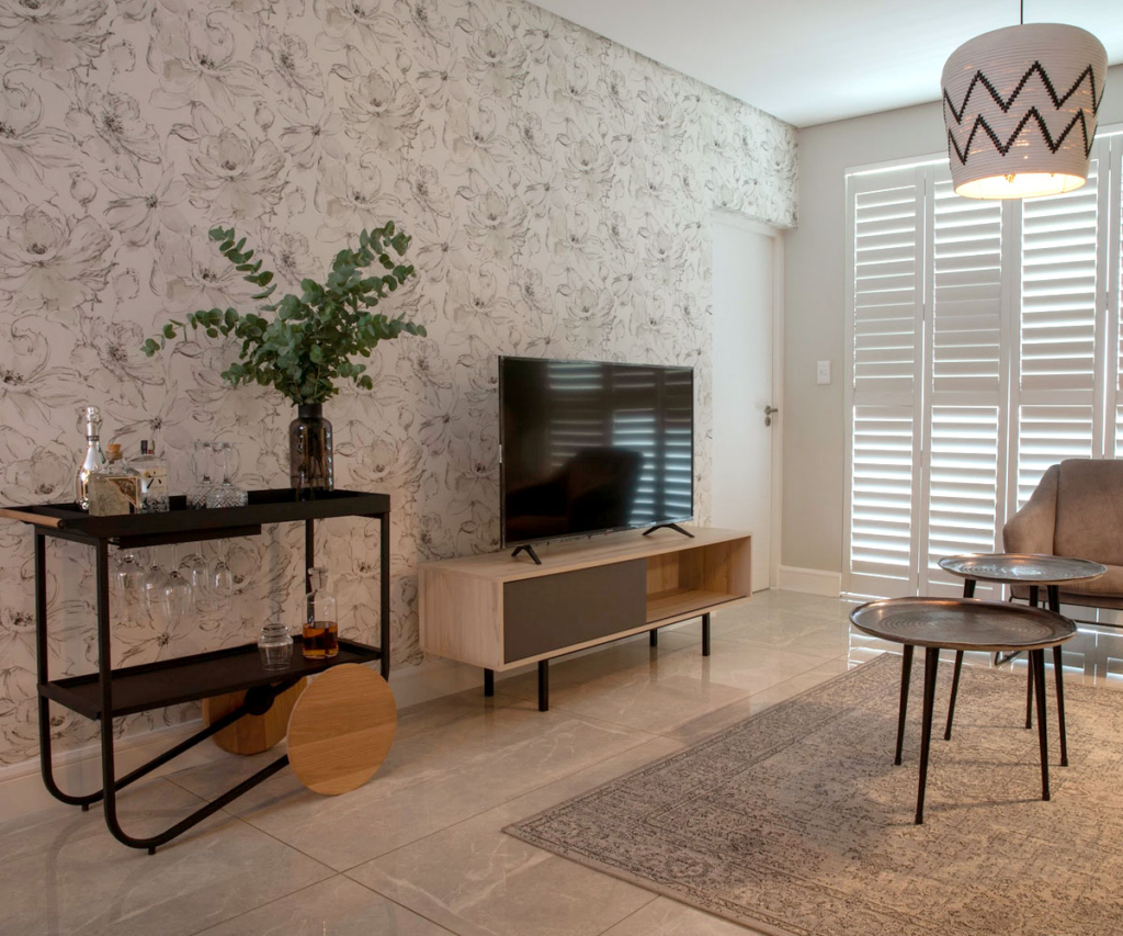 Monochromatic bar cart and media unit set against floral botanical wallpaper in a Serengeti Estate apartment.