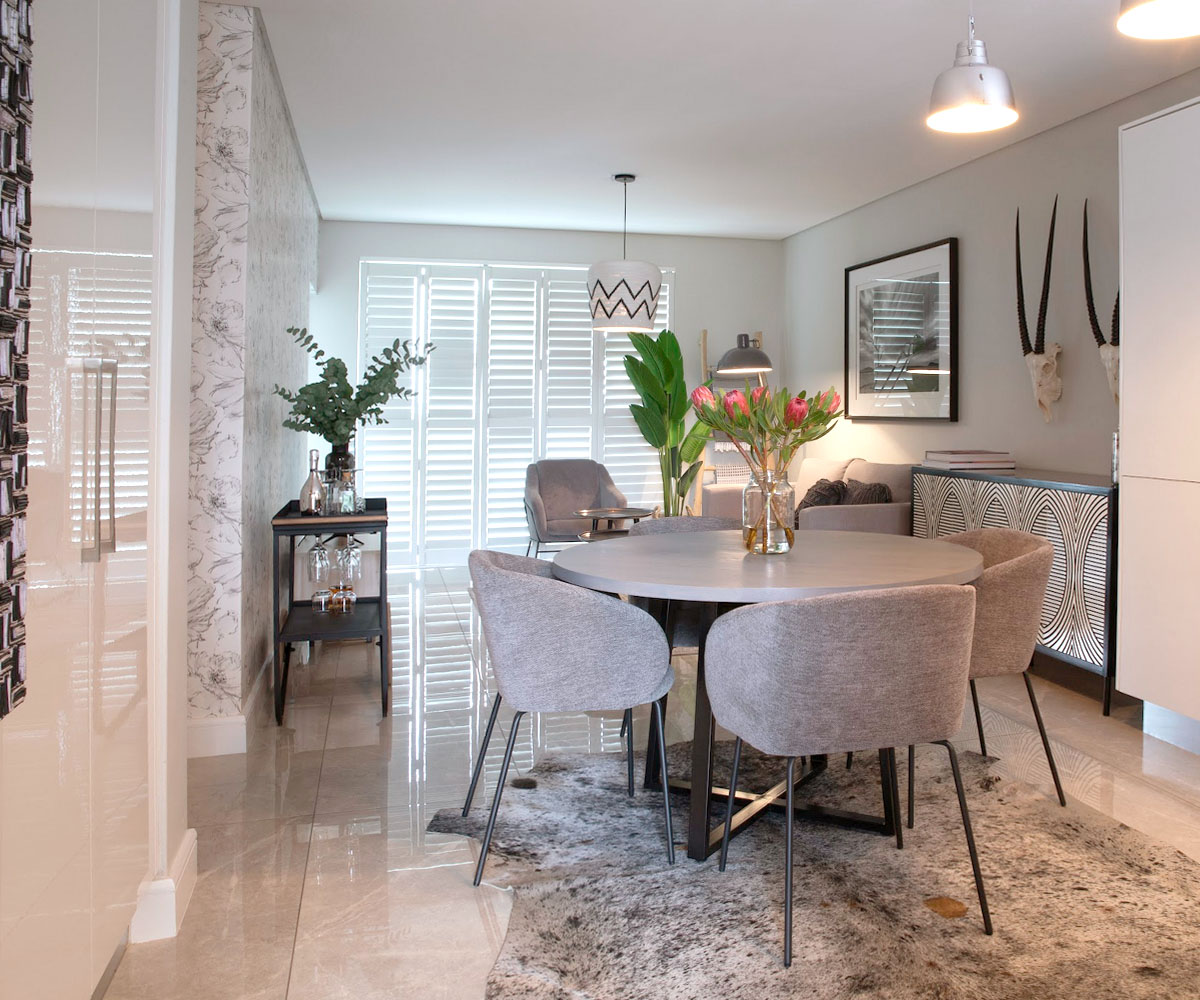 Open-plan dining and living area at Serengeti Estate featuring a natural hide rug, round grey dining table, and monochrome botanical wallpaper.